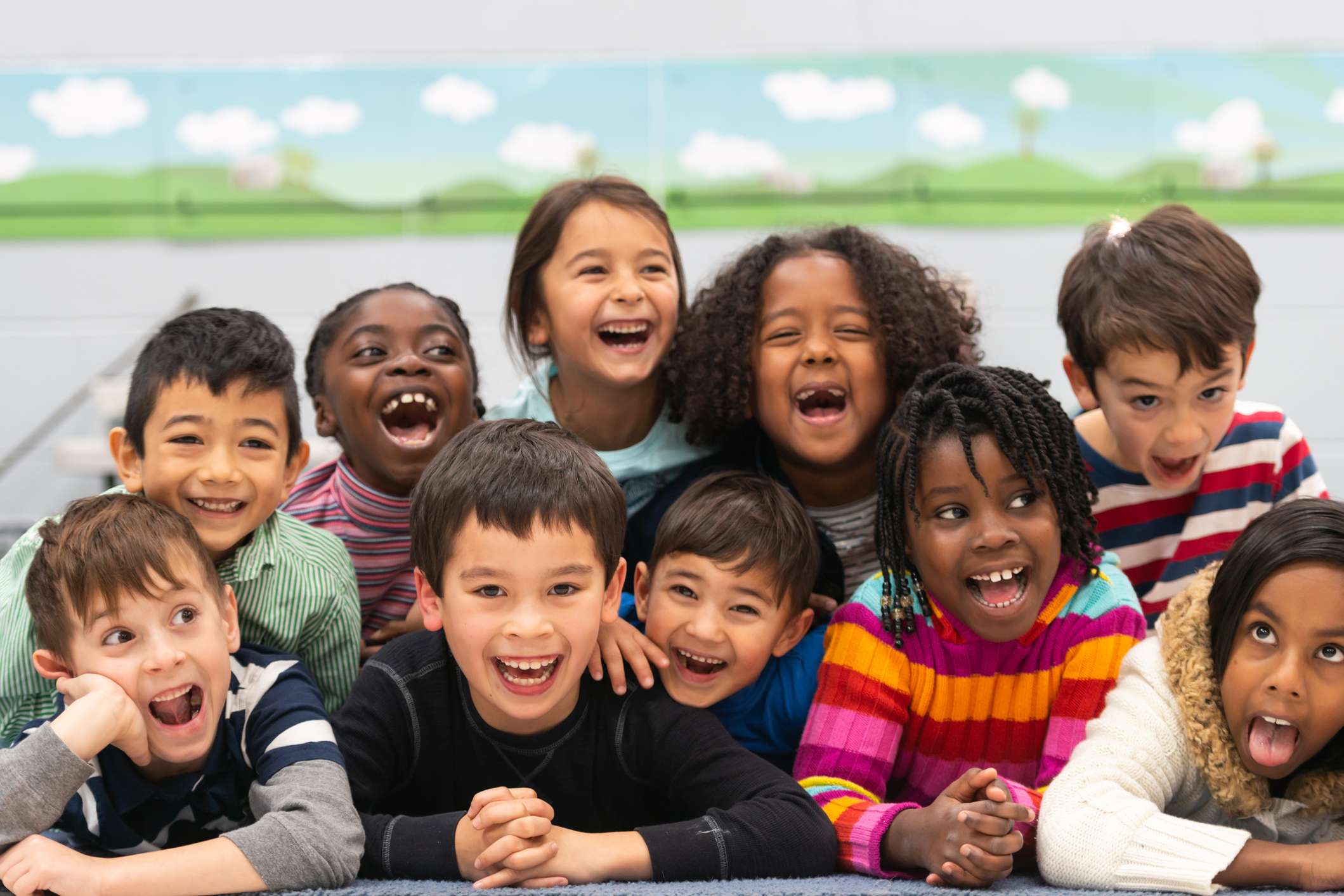 A group of diverse kids smile in this portrait. They are stacked on top of each other while cuddling in close and showing how happy they are.