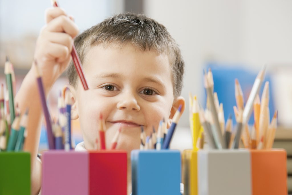 Child picking up colored pencil in school classroom