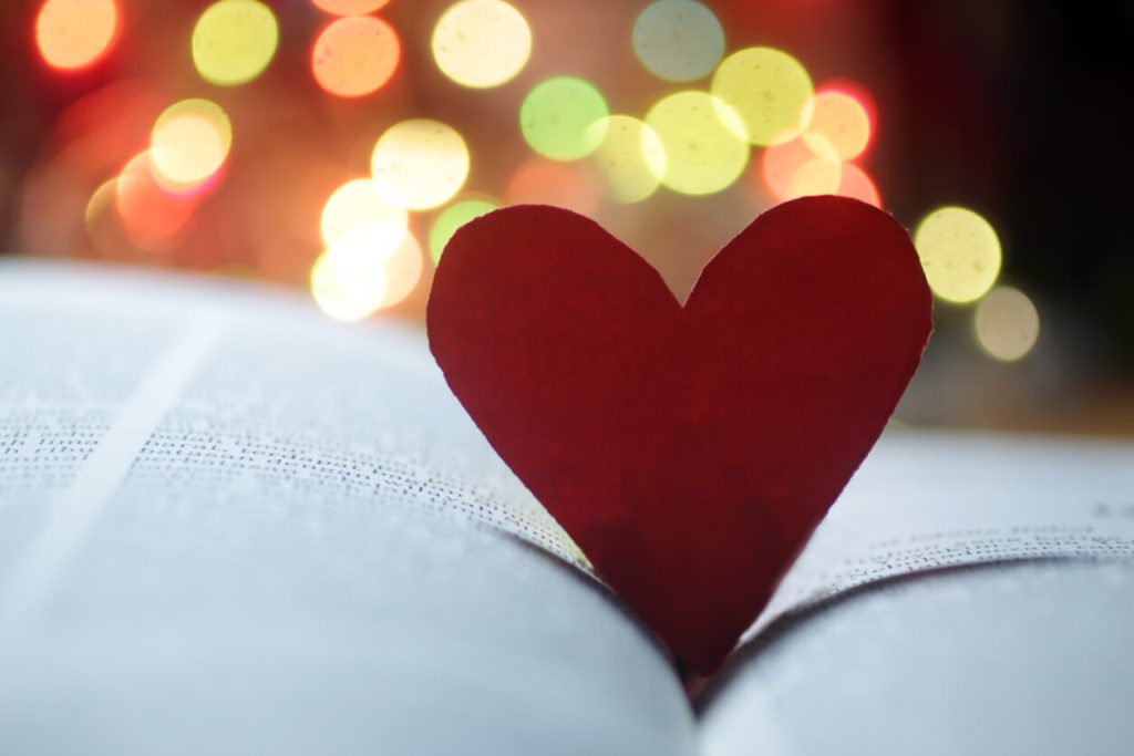 A little paper heart sticking out of a Bible with soft, round lights in the background