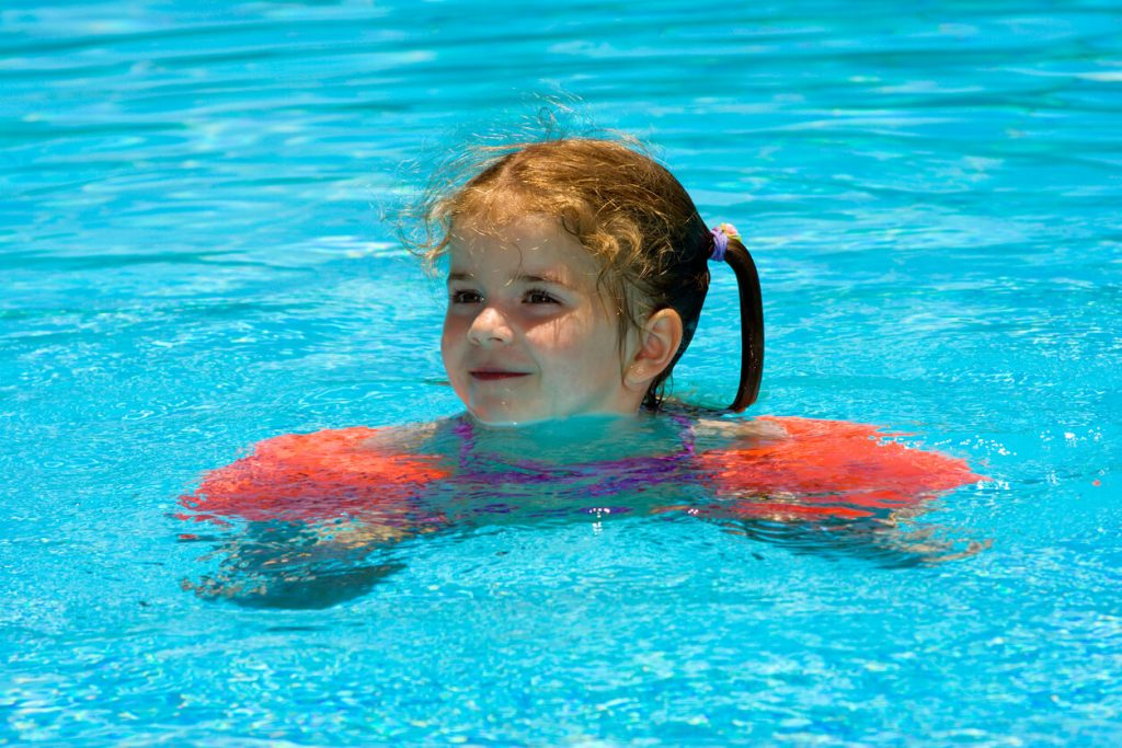 A little girl in a pool wearing floaties