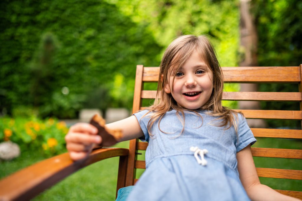 A little girl smiling in a garden chair while eating her cookie