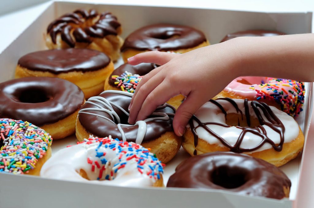 A kid picking a donut out of the box filled with tasty looking donuts