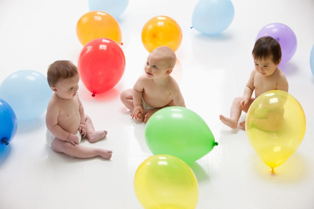 A bunch of babies sitting among colorful balloons