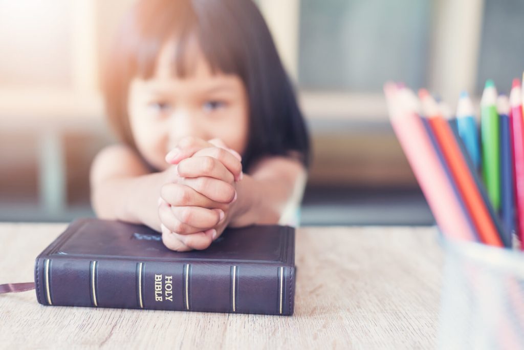 A little girl folding her hands in prayer over a Bible