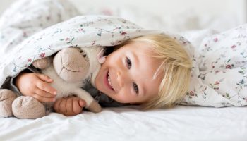 A blond little girl snuggling a stuffed animal under a comforrter