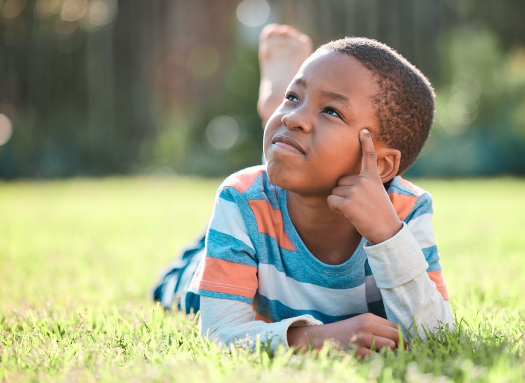 A little boy is pondering things as he lays on his stomach in the grass
