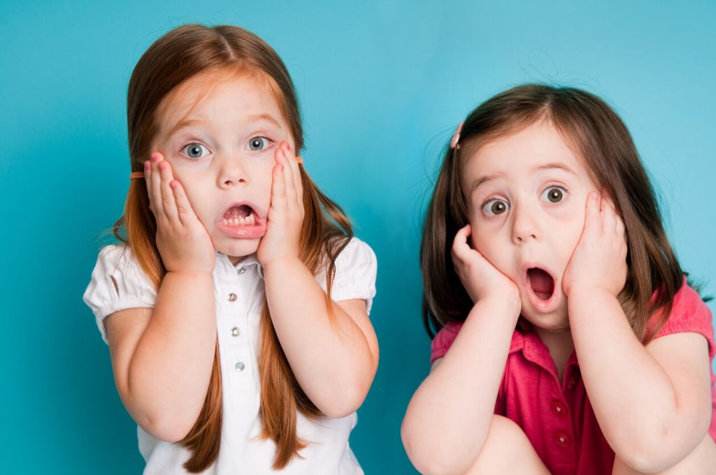 Two little girls holding their faces in shock with their mouths gaping