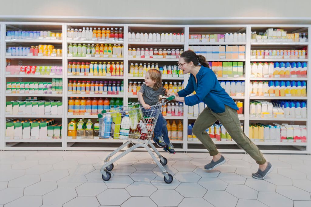 A mom running while pushing her son in a cart. Both of them are having fun as they run down the store aisle