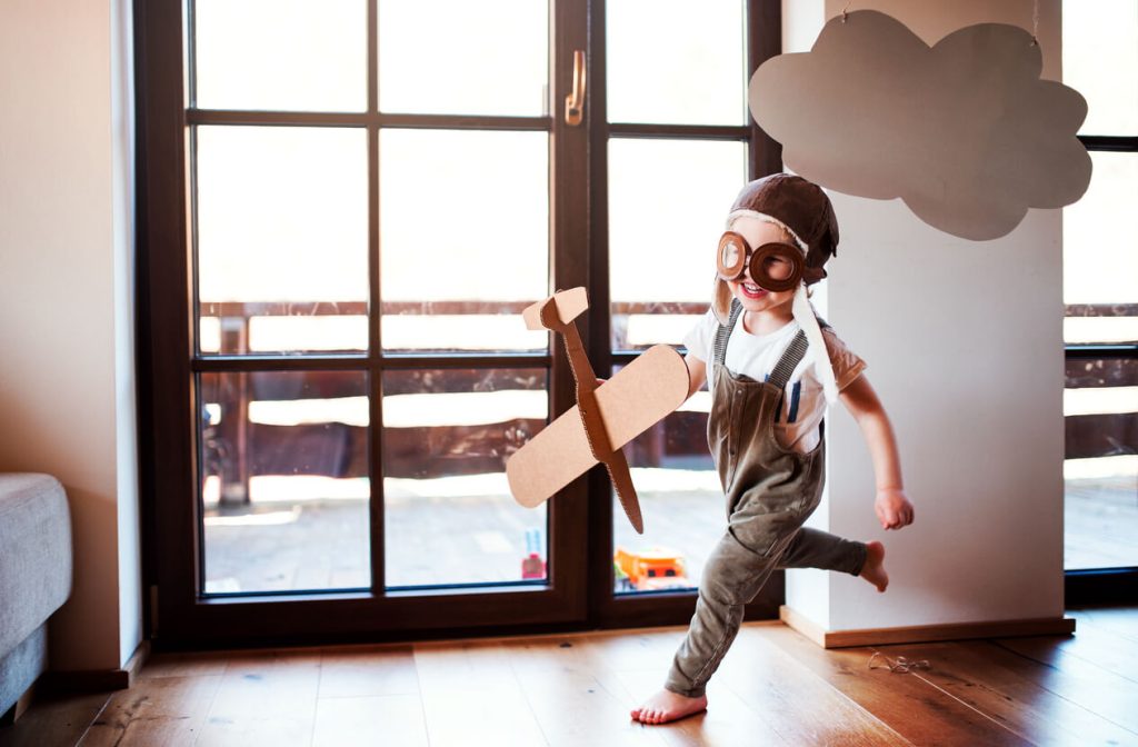 A little boy running around his house with a cardboard airplane and a cutout cloud above him.