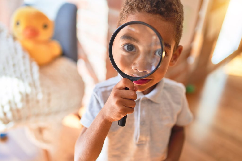 Little boy looking up at viewer with a magnifying glass
